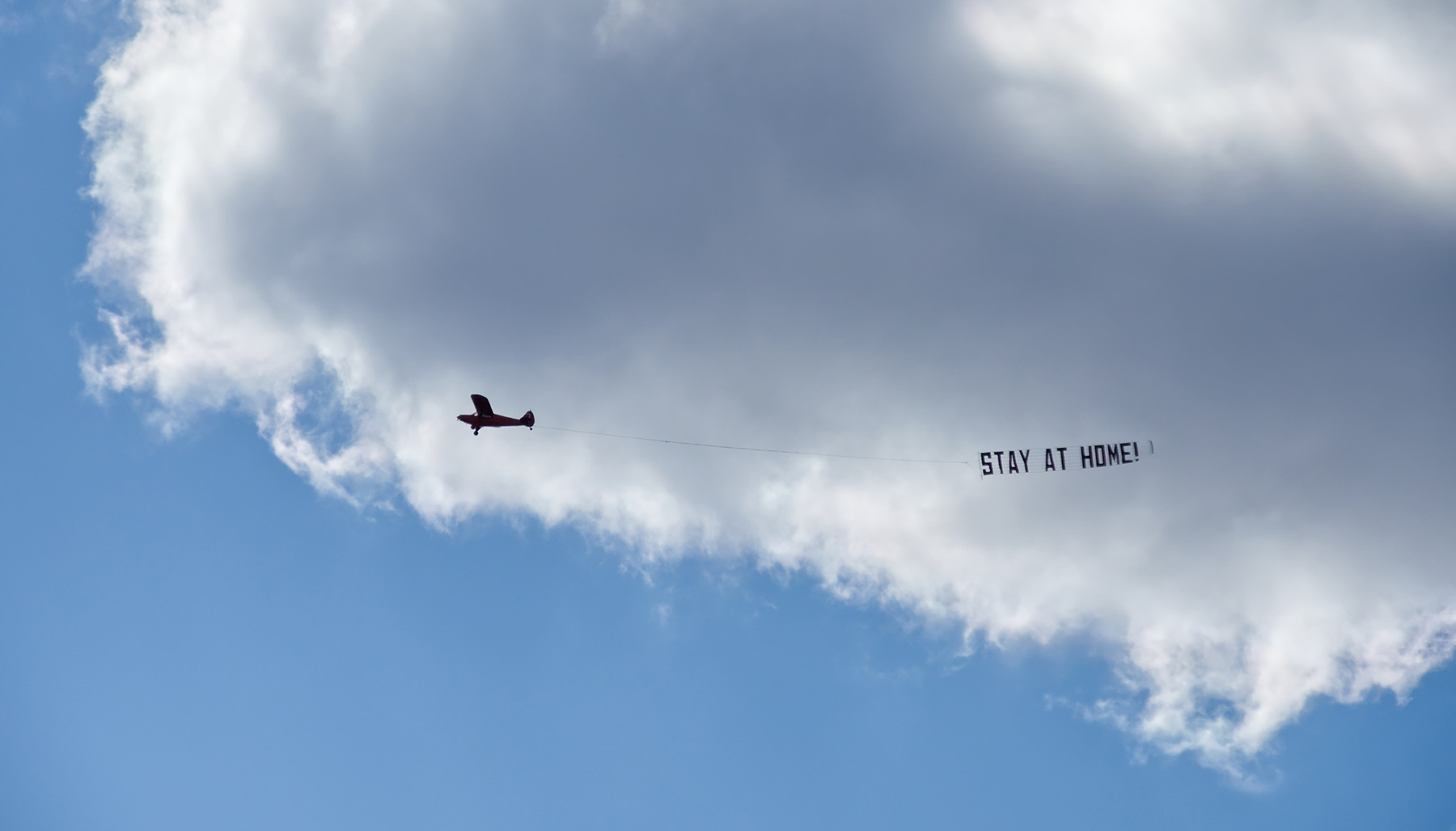 airplane flying and towing a sign behind it that says "stay at home"